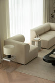 Modern living room with beige sofa and armchair, side tables, and a rug.