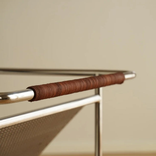 Close-up of a metal and leather handle on a chair against a beige wall.