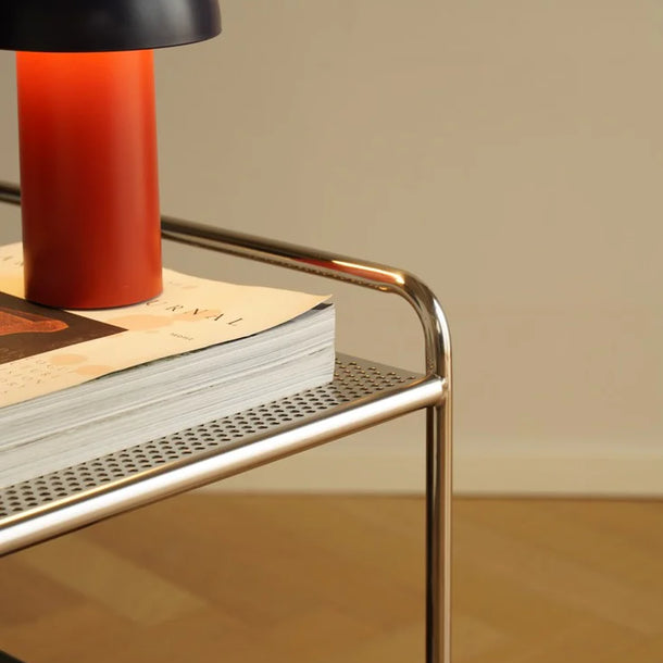 Modern bar cart with a red and black lamp and books on a wooden floor.