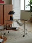Modern interior with a metal trolley, black lamp, and books in a room with wooden cabinet and window.