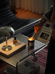 Person lighting a candle on a table with a lamp and book in the background
