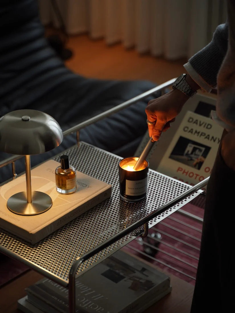 Person lighting a candle on a table with a lamp and book in the background