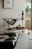 Modern bar cart with wine, glasses, and books in a living room setting.