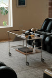 Metal serving cart in a living room setting with a black armchair and window in the background.