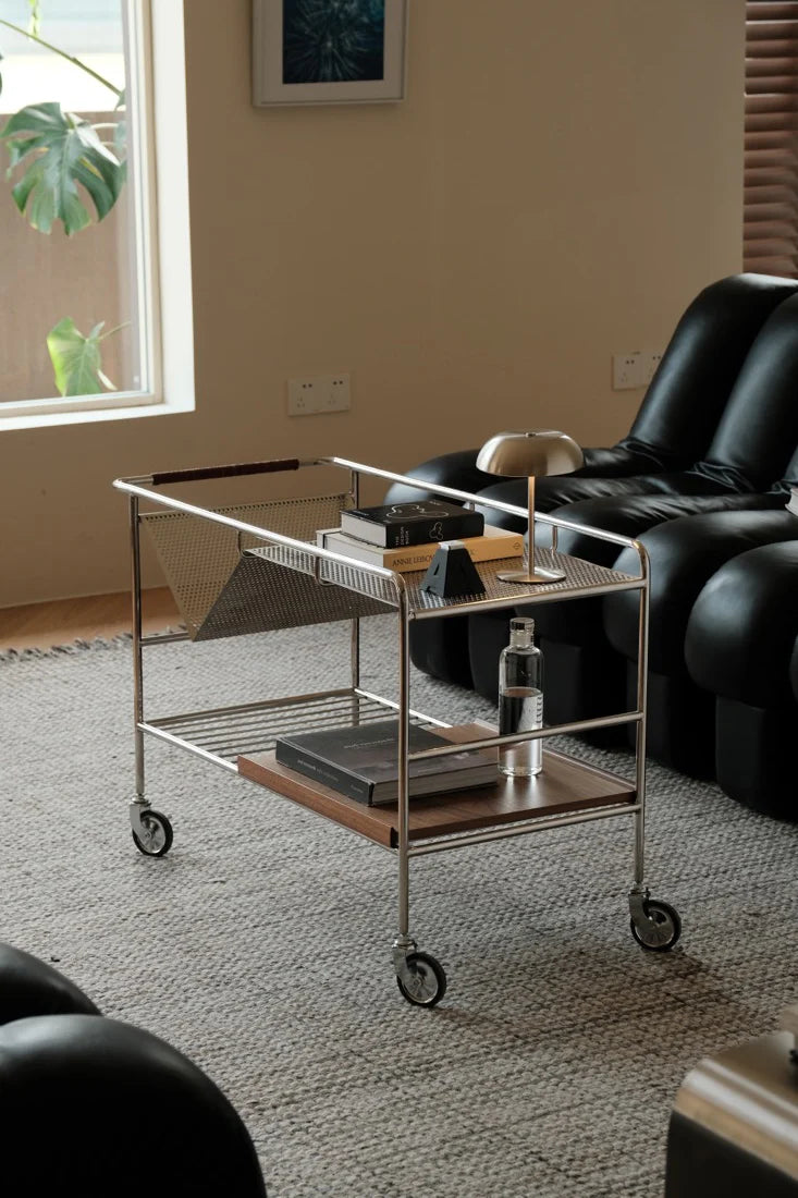 Metal serving cart in a living room setting with a black armchair and window in the background.