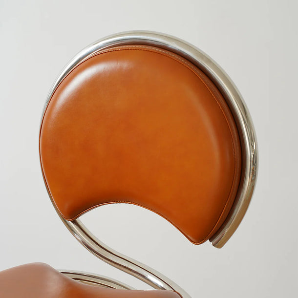 Close-up of a brown leather chair with a metallic frame on a light gray background