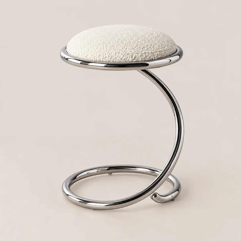 A modern stool with a textured off-white circular seat cushion and a curved, polished chrome metal base, set against a solid light beige background.