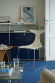 Modern interior with a blue sideboard, white chair, and glass table.