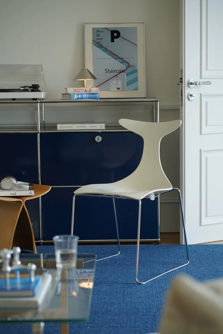 Modern interior with a blue sideboard, white chair, and glass table.