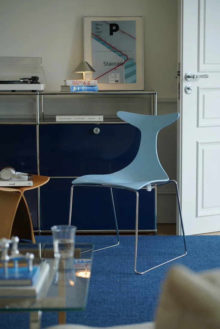 Modern office space with a blue chair, glass table, and framed map on a shelf.
