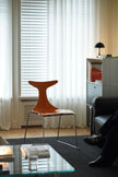Modern living room with a wooden chair, glass coffee table, and a person sitting on a sofa.