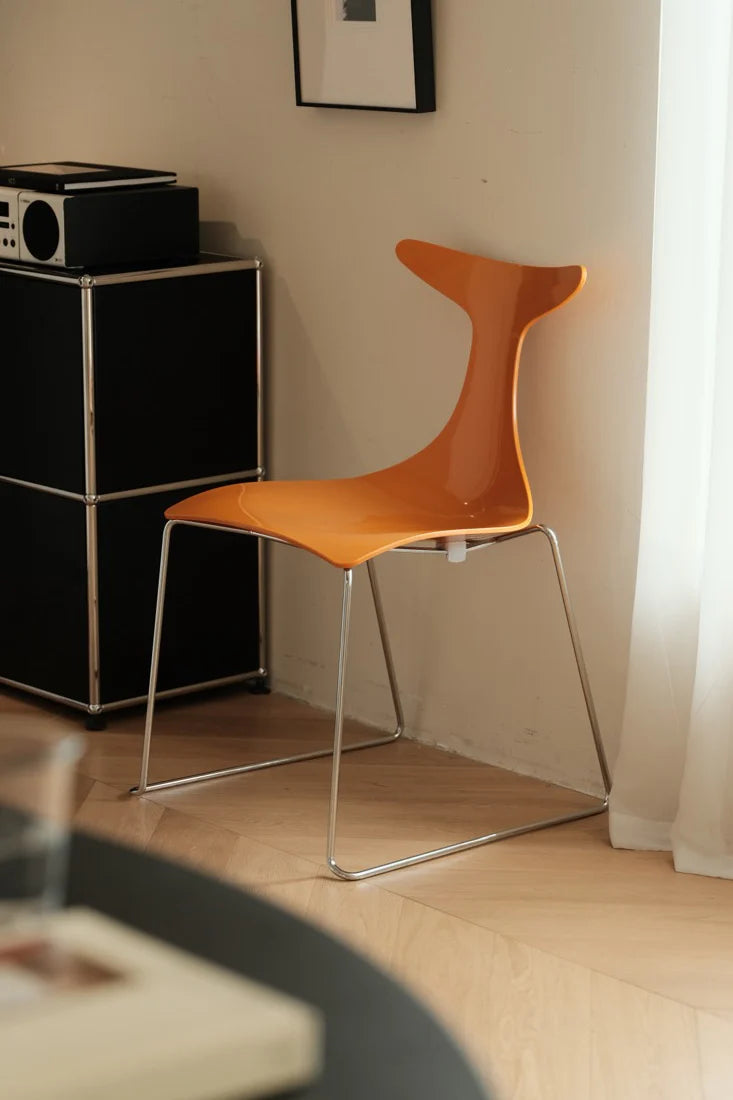 Orange chair in a room with a black cabinet and white curtain.