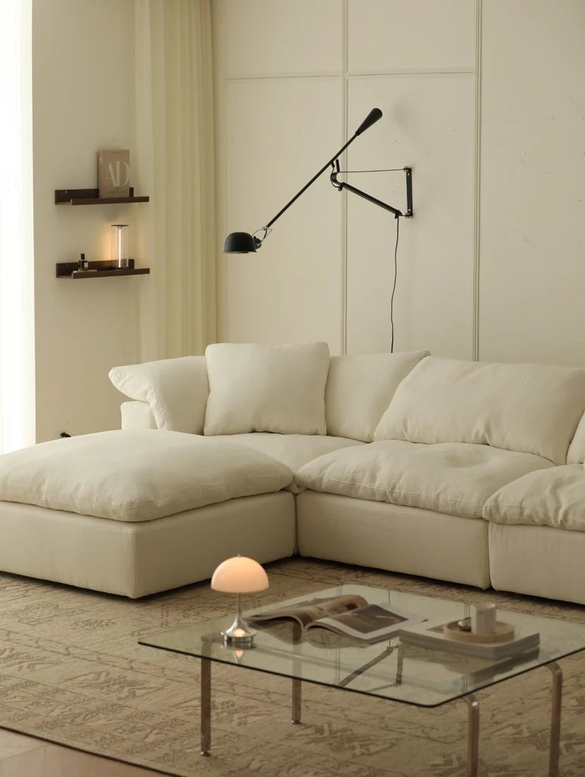 Beige sectional sofa in a living room with a glass coffee table and wall-mounted lamp.