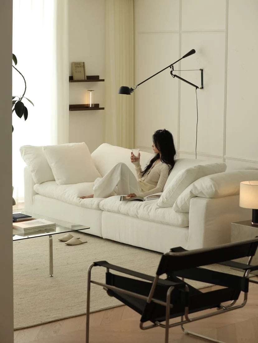 Woman sitting on a white sofa in a modern living room with a lamp and plant.