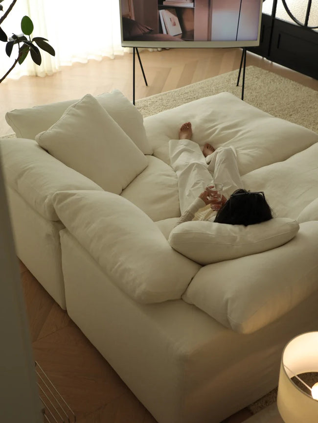 Person lying on a large white sofa watching TV in a cozy living room.