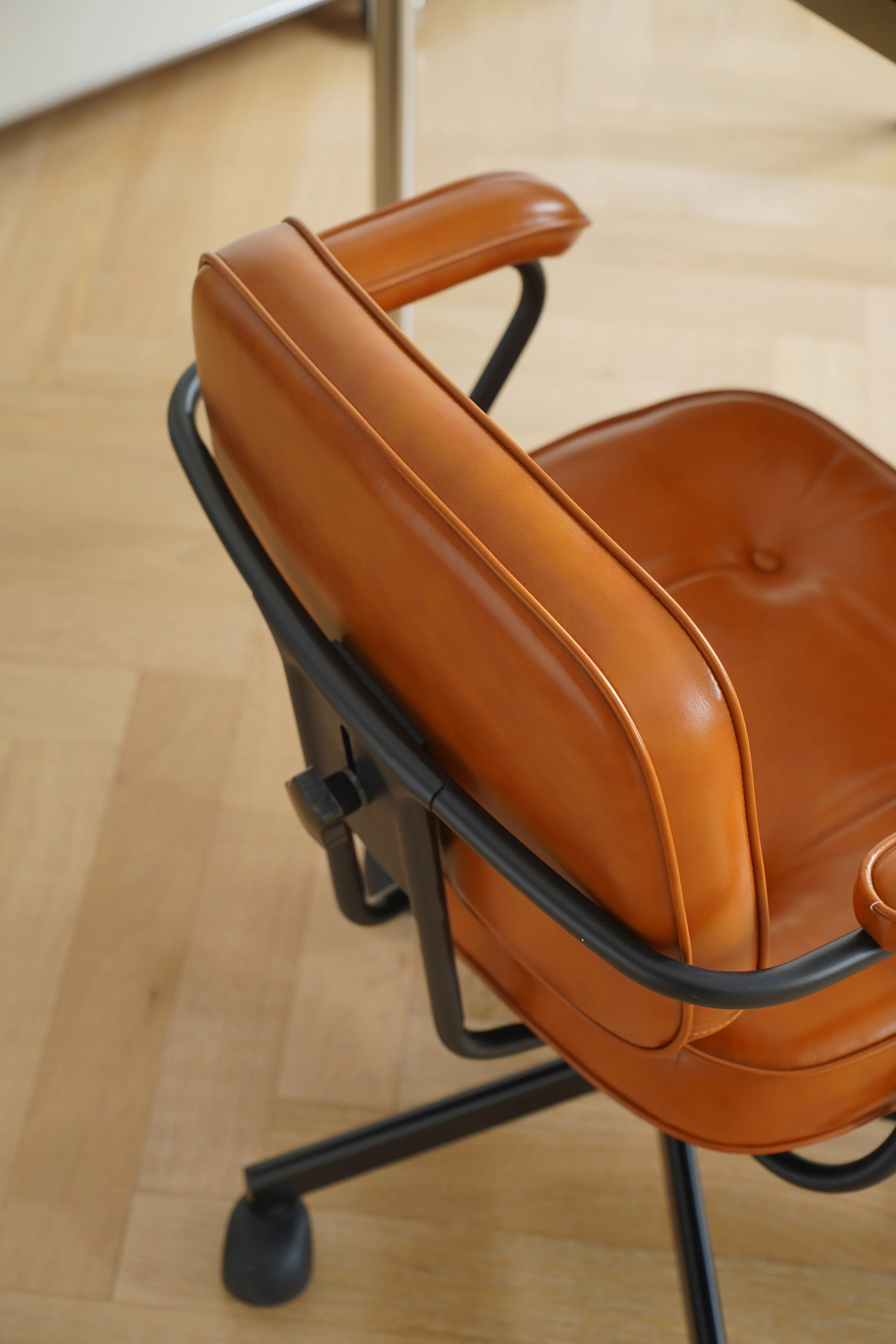 Brown leather office chair with black metal frame on a wooden floor