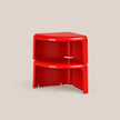 A pair of bright red, modular plastic corner side tables stacked together, set against a solid light beige background.