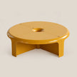 A modern low-profile round coffee table in a glossy mustard yellow finish, featuring a central circular cutout and integrated legs, set against a solid light beige background.