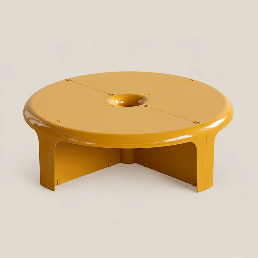 A modern low-profile round coffee table in a glossy mustard yellow finish, featuring a central circular cutout and integrated legs, set against a solid light beige background.