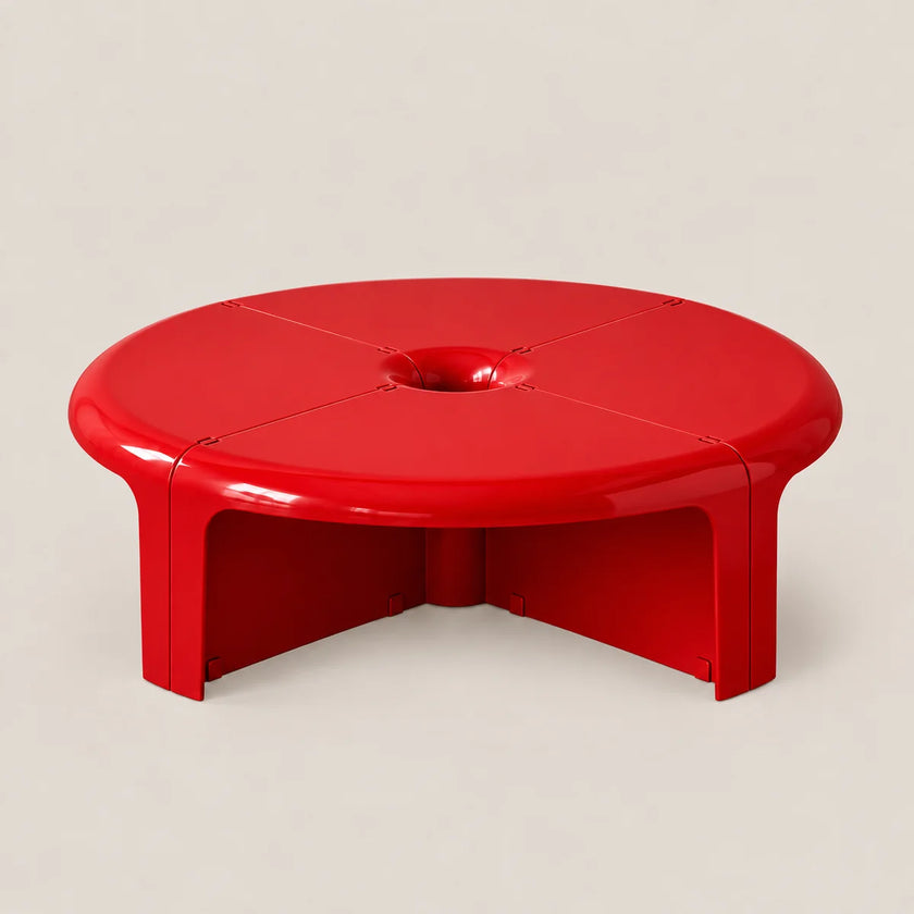 A bright red, low-profile round coffee table with a glossy finish, featuring a central circular cutout on the tabletop and a geometric open base, set against a plain light beige background.
