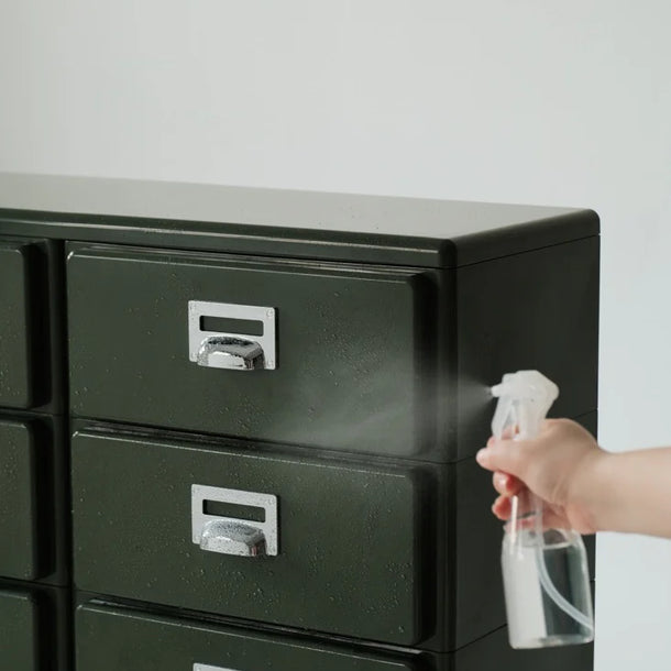 Person cleaning a black metal file cabinet with a spray bottle.