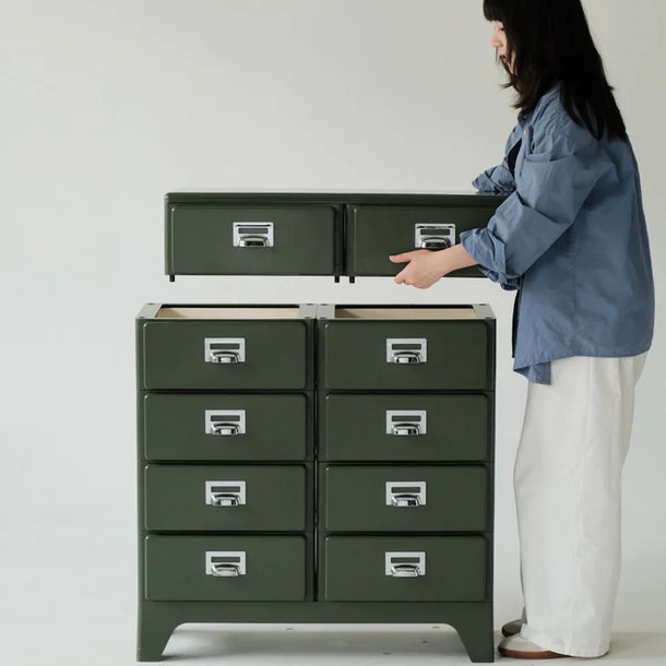 Person interacting with a green metal cabinet with multiple drawers on a white background