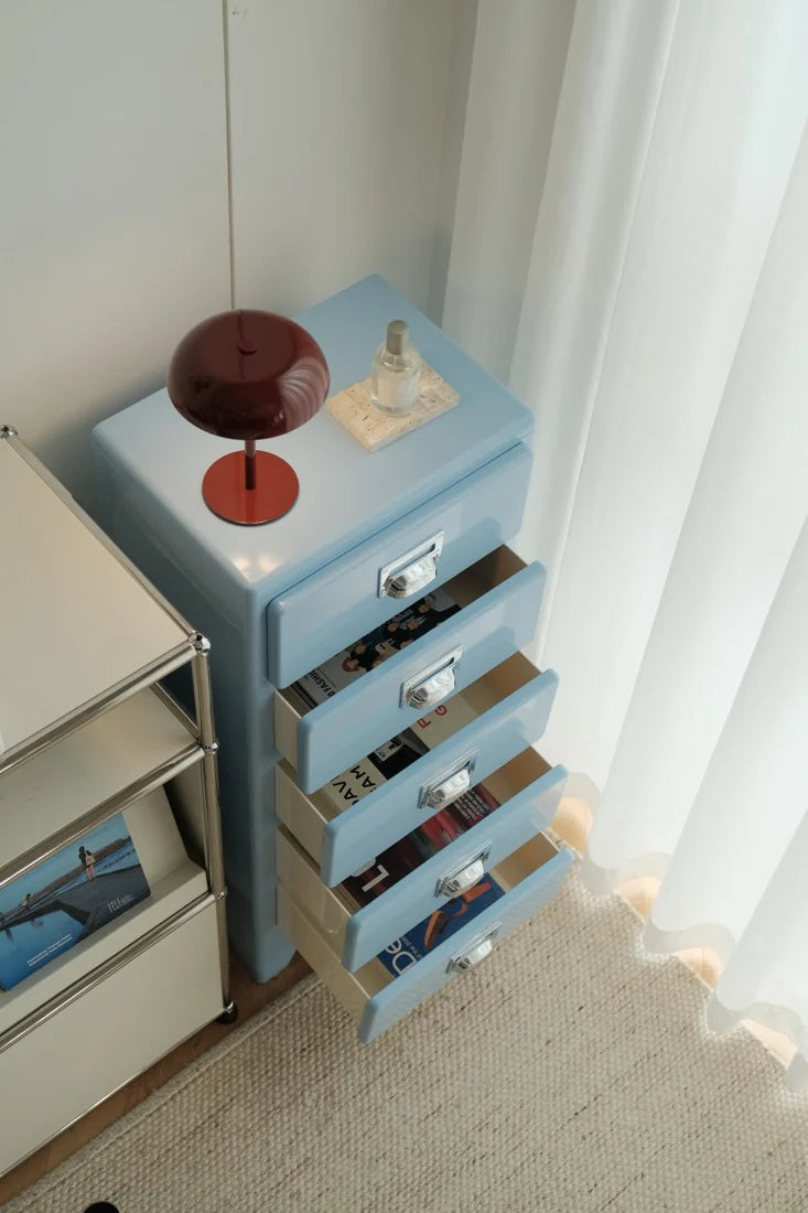 Blue dresser with open drawer in a room with white curtains.