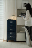 Person reading a book next to a blue filing cabinet in a room with white walls and a window.