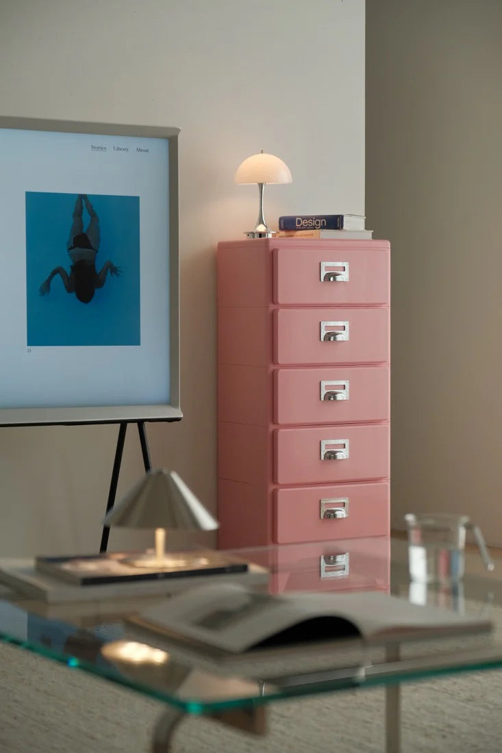 Pink filing cabinet next to a glass desk with a lamp and framed picture in an office setting.