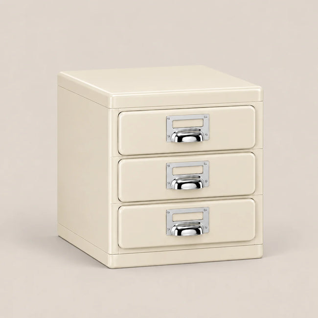 A cream-colored three-drawer metal file cabinet with silver pull handles, shown on a solid light beige background.