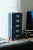 Blue filing cabinet with four drawers in a room with a TV and lamp.