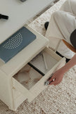 Person opening a drawer in a small table with items inside.