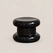 A glossy black modern stool with a tiered, rounded design, photographed against a solid light beige background.