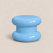A glossy light blue plastic knob or dial with a rounded mushroom-shaped design, set against a solid beige background.
