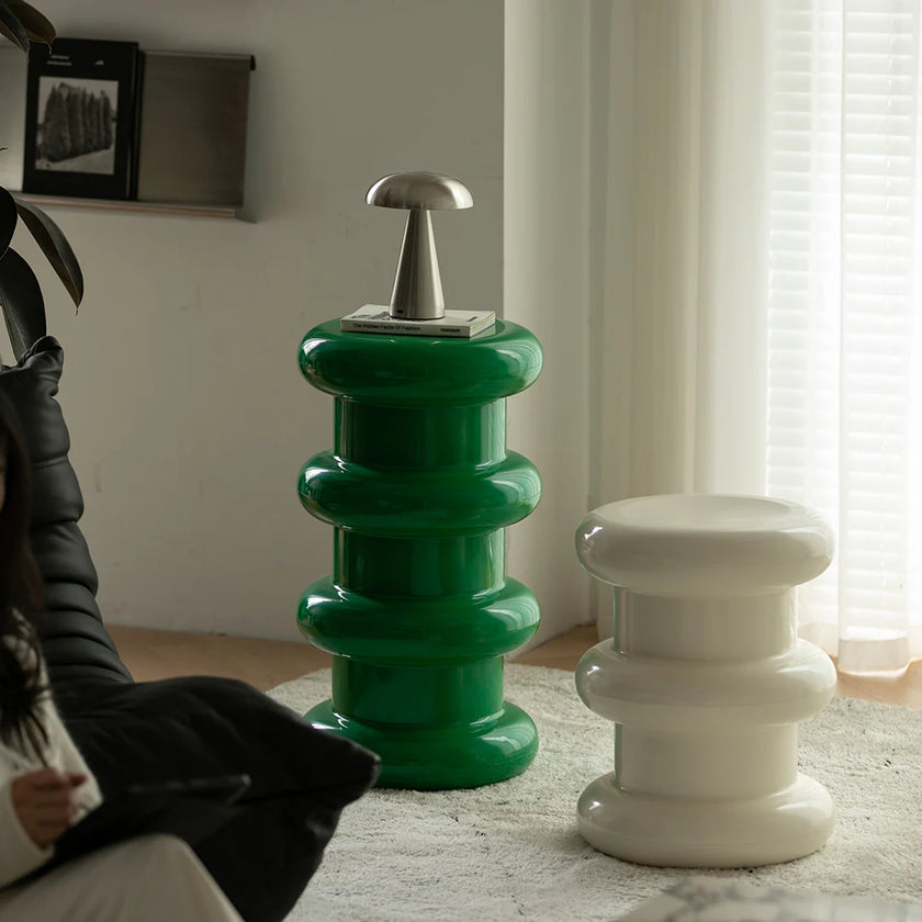 Two unique stools, one green and one white, in a room with a window and chair.