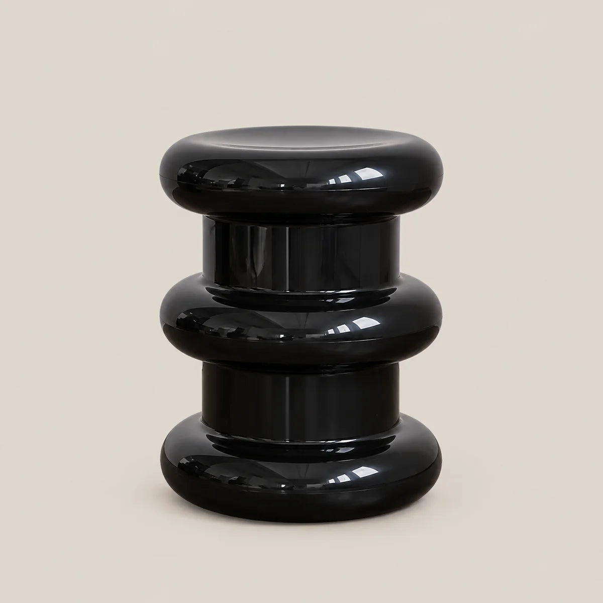 A glossy black modern side stool with a stacked, tiered circular design, photographed against a solid light beige background.