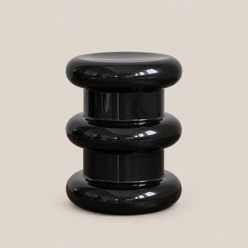 A glossy black modern side stool with a stacked, tiered circular design, photographed against a solid light beige background.