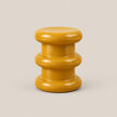 A glossy mustard yellow side stool with a stacked, rounded modern design, photographed against a solid light beige background.
