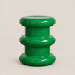 A glossy green modern stool with a stacked, rounded tiered design, photographed against a solid light beige background.