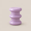 A small round side table with a glossy lavender purple finish, featuring three stacked circular tiers, set against a solid beige background.