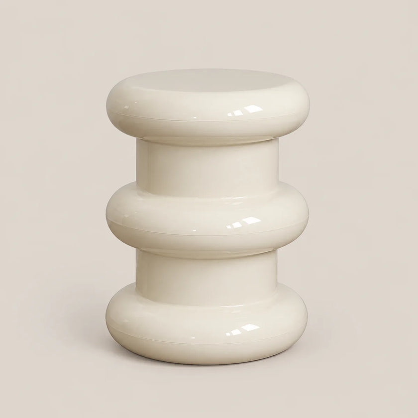 A glossy, modern side stool with a stacked, rounded organic design in a warm off-white/cream color, set against a solid light beige background.