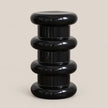 A glossy black modern pedestal stool with stacked, rounded cylindrical tiers on a light beige background.