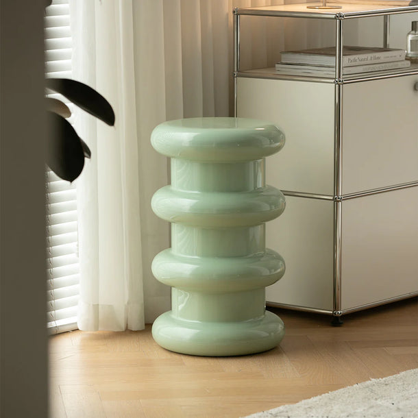 Green cylindrical stool in a room with a metallic cabinet and white curtains.
