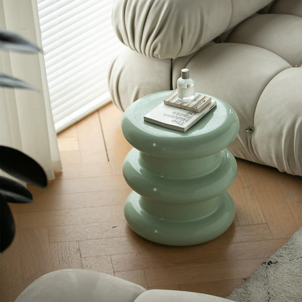 Green side table with a bottle and book on a wooden floor next to a beige sofa.