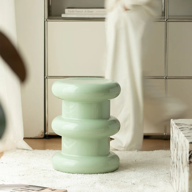 Light green stool with stacked design on a white rug in a room setting