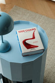 Book titled '1000 Chairs' on a blue side table with a lamp.