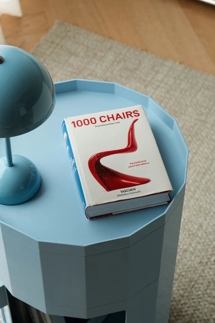 Book titled '1000 Chairs' on a blue side table with a lamp.