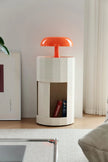 Modern cylindrical side table with a red lamp shade in a room setting.