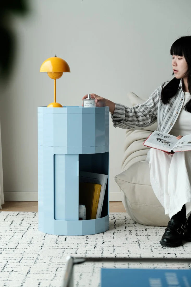 Woman reading a book next to a blue side table with a yellow lamp in a modern living room.