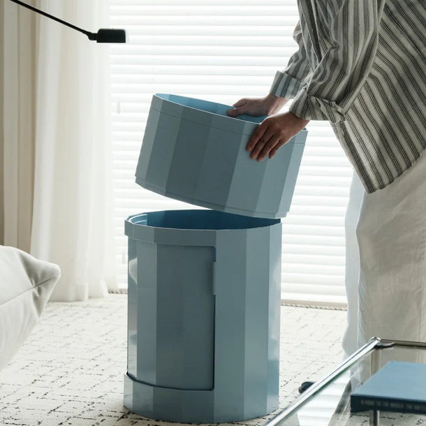Person interacting with a blue cylindrical container in a room with light-colored walls and furniture.